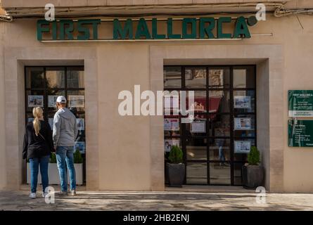 Santanyi, Spanien; dezember 11 2021: Hauptfassade des Immobilienunternehmens First Mallorca, mit ein paar Touristen, die Anzeigen in seinen s betrachten Stockfoto