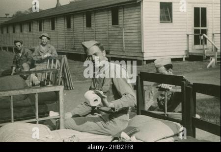 Antikes Foto aus dem Jahr c1950, Soldat der Armee nach dem Zweiten Weltkrieg, der Toilettenpapier vor der Kaserne hielt. Die Gruppe der Soldaten entfernt oder installiert Fenster im Gebäude. Genaue Lage unbekannt, USA. QUELLE: ORIGINAL-FOTODRUCK. Stockfoto