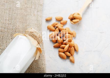 Mandelmilch in einer Flasche mit einer Handvoll Körner und einem Holzlöffel mit einem Sackleinen Tuch auf einem hellen Hintergrund. Draufsicht Stockfoto