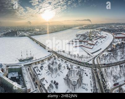 Drohne Sicht des Winters St. Petersburg bei Sonnenuntergang, gefrorener Neva Fluss, Dampf über der Stadt, Peter und Paul Festung, Autoverkehr auf Trinity Brücke Stockfoto