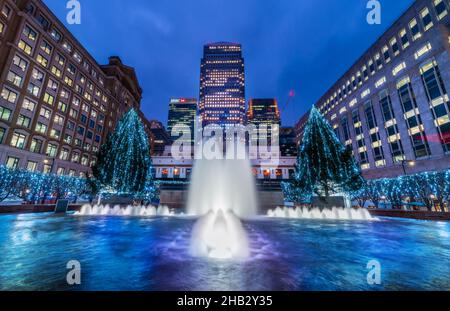 London, England, Großbritannien - 15. Dezember 2021: Blick auf den Cabot Square und den künstlerischen Brunnen, der in Abendlichtern beleuchtet wird, umgeben von Weihnachten de Stockfoto