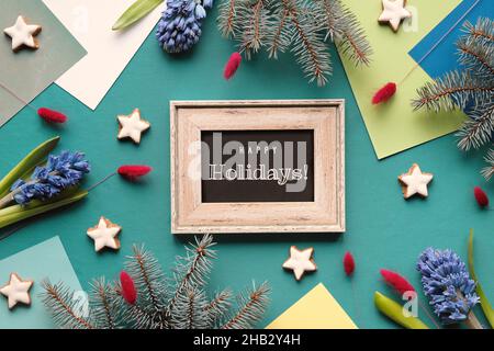 Text Frohe Feiertage auf Tafel. Grün geschichtete geometrische Papier Hintergrund mit Stern Cookies, blauen Hyazinthen Blumen und Tannenzweigen. Winter saisonal Stockfoto