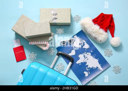 Koffer mit Weihnachts-Geschenkboxen, Sonnenbrille, Weltkarte und Weihnachtsmütze auf blauem Hintergrund Stockfoto