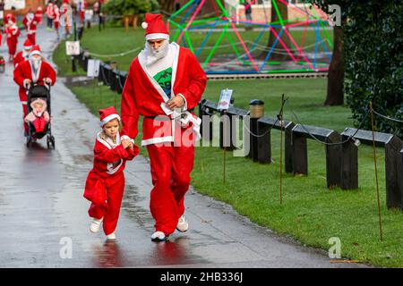 Mann und Tochter halten sich die Hände, während sie in einem Santa Dash Rennen Stockfoto