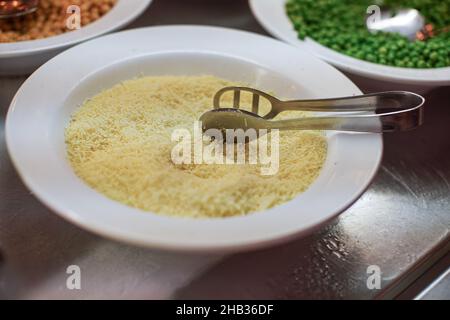 Weißer Teller mit geriebenem Käse im Buffetrestaurant, Details aus der Nähe Stockfoto