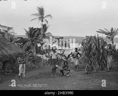 In Native Village bei Suva, Fidschi, Burton Brothers Studio, Fotostudio, Juli 1884, Schwarz-Weiß-Fotografie, drei Männer und eine Frau mit einem Baby stehen, zwei Männer hocken in einem Clear. Das Meer ist im Hintergrund sichtbar Stockfoto