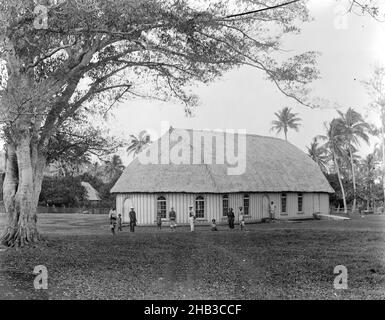 Neiafu, Wesleyan Church (außen), Burton Brothers Studio, Fotostudio, 26. Juli 1884, Neuseeland, Schwarz-Weiß-Fotografie, großer Baum links im Vordergrund auf Lichtung vor dem Kirchengebäude. Zehn Menschen stehen oder sitzen vor der Kirche. Die Kirche hat ein traditionelles Fale-Dach mit Holzwänden, Türen und Fenstern im Kolonialstil. Hohe Kokospalmen befinden sich hinter der Kirche, das Dach eines anderen Gebäudes ist in tropischem Laub direkt hinter dem Baum zu sehen Stockfoto