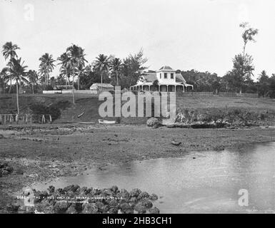 The King's Palace, Neiafu, Vavau, Tonga, Burton Brothers Studio, Fotostudio, Juli 1884, Neuseeland, Schwarz-Weiß-Fotografie, Felsenvorland im Vordergrund, mit Ebbe und Ruderboot am unteren Rand des Bankenzentrums. Hill hat ein zweistöckiges Kolonialgebäude mit Veranda im Erdgeschoss und einem großen Turm im zweiten Stock (Mitte). Andere Gebäude links und ein Zaun rennt herum. Kokospalmen umgeben Stockfoto