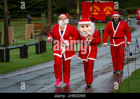 Menschen laufen in einem Santa Dash, einer trägt eine große Gesichtsmaske Stockfoto