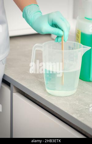 Die Kosmetikerin mischt Desinfektionsmittel mit einem Stick ins Wasser. Sterilisation von Werkzeugen Stockfoto