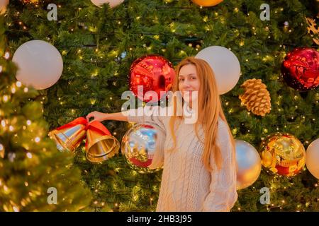 Lächelnde Frau mit großen glänzenden Kugeln, die Glocken am weihnachtsbaum hängen Stockfoto