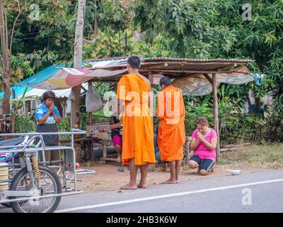 Buddhistische Mönche, die am frühen Morgen in Sam ROI Yot südlich von Hua hin in Thailand Almosen von thailändischen Frauen erhalten. Stockfoto