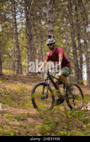 Ein hübscher und fitte Kerl, der in einem roten Hemd gekleidet ist, fährt alleine mit dem Fahrrad und versucht, mit der Gruppe Schritt zu halten Stockfoto