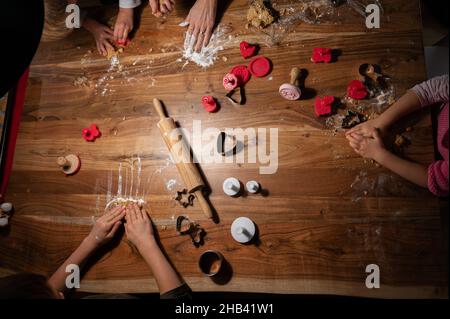 Draufsicht auf eine Familie, die Weihnachtsferien machte, geformte vegane Kekse auf einem Holztisch. Stockfoto