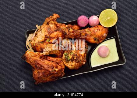 Draufsicht auf Tandoori Chicken mit Chutney und Zwiebeln auf dem Teller, berühmtes indisches Essen Tandoori Murga Stockfoto