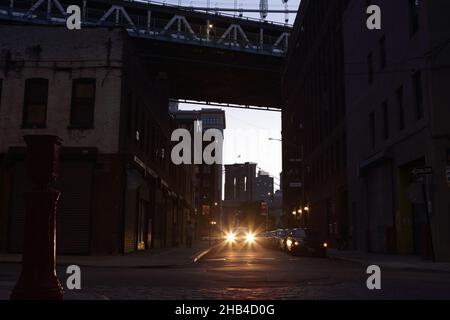 Dunkle Brooklyn Street bei Nacht unter den Brücken von Manhattan und Brooklyn mit Autoscheinwerfern und Silhouetten. Hintergrund mit langer Belichtung und Retro-Look. Stockfoto