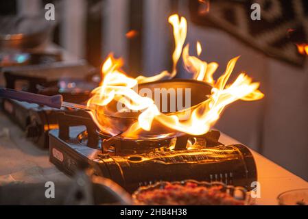 Kupferpfanne, die auf dem Kochbrenner am Outdoor Resort Buffet in Flammen aufgegangen ist Stockfoto