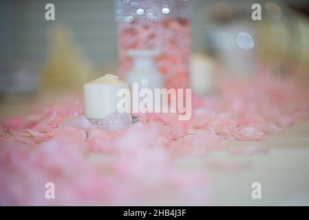 Weiße Teelicht-Kerze, umgeben von rosa Blumenpedalen am Hochzeitstisch Stockfoto