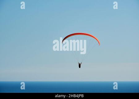 Der Gleitschirm schwebt hoch im Himmel über dem blauen Meer. Extreme Sporthintergründe Stockfoto