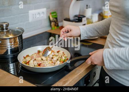 Seitenansicht auf unbekannte kaukasische Frau mit Kochpfannenherstellung Vegane oder vegetarische gesunde Mahlzeit zu Hause Stockfoto