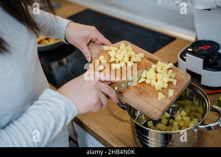 Nahaufnahme der Hände einer unbekannten Frau, die Schneidebrett hält In der Küche setzen Stücke von Kartoffeln in die Vegane oder vegetarische Suppenküche gesund mir Stockfoto