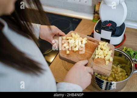 Nahaufnahme der Hände einer unbekannten Frau, die Schneidebrett hält In der Küche setzen Stücke von Kartoffeln in die Vegane oder vegetarische Suppenküche gesund mir Stockfoto