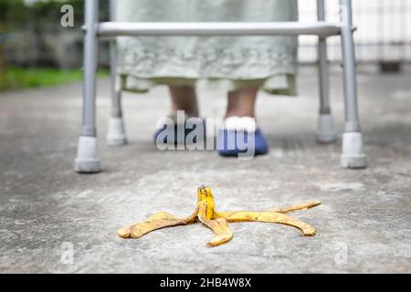 Achtlose ältere Frau tritt über eine Bananenschale auf dem Gehweg Stockfoto