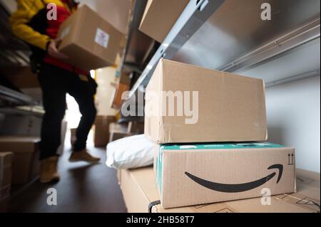 Ober Ramstadt, Deutschland. 15th Dez 2021. Ein Paket des Online-Händlers Amazon steht in einem DHL-Transporter zur Paketzustellung. Im Hintergrund sortiert ein DHL-Mitarbeiter seine Pakete zur Auslieferung. Quelle: Sebastian Gollnow/dpa/Alamy Live News Stockfoto