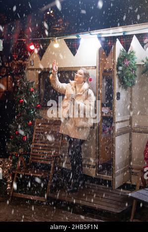 Offen junge Frau in voller Höhe Freude entspannend Fang Schneeflocken und Tasse Kakao Getränk in der Hand hält an glücklichem Neujahr und heiligabend ni Stockfoto