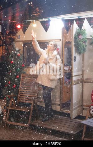 Offen junge Frau in voller Höhe Freude entspannend Fang Schneeflocken und Tasse Kakao Getränk in der Hand hält an glücklichem Neujahr und heiligabend ni Stockfoto