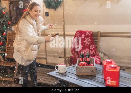 Moskau 11.29.2021. Frau hält Hände Smartphone und Foto für Blog eines Tisches mit Getränken am glücklichen Neujahr und weihnachten Winterferien Vorabend Stockfoto