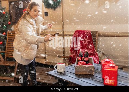 Moskau 11.29.2021. Frau hält Hände Smartphone und Foto für Blog eines Tisches mit Getränken am glücklichen Neujahr und weihnachten Winterferien Vorabend Stockfoto