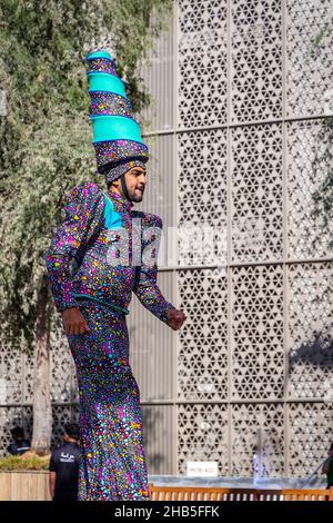 Dubai, VAE, 09.12.2021. Mann auf Stelzen in farbenfroher Kleidung und Hut während der Expo 2020 Dubai Daily Parade. Stockfoto