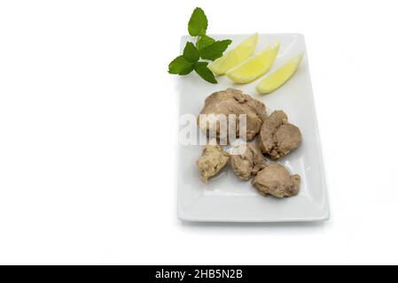 Dorschleber in seinem Öl auf einem Teller mit Zitronenscheiben und grünen Blättern, Draufsicht, weißer Hintergrund Stockfoto