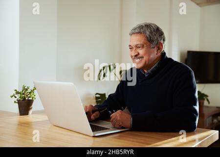 Multikultureller älterer Mann, der lächelt, während er online mit der Familie telefonieren kann. Isoliert in einem modernen Zuhause, sitzend an der Küchentheke. Stockfoto