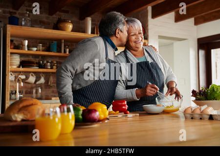 Biracial ältere Paar glücklich Kochen in der modernen Küche. Ehemann küsst Frau auf der Wange, gesund im Ruhestand. Stockfoto