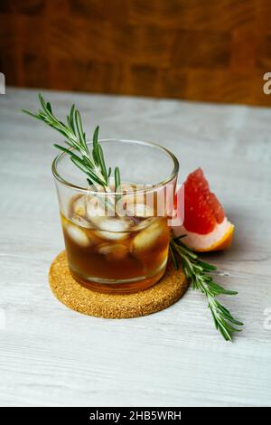 Whiskey-Sour-Cocktail mit Rum-Eis-Grapefruit und Rosmarin in Schrotglas. Alkoholcocktail auf Holztisch Stockfoto
