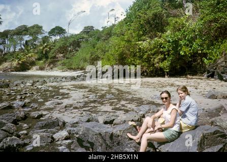 Zwei ausländische britische Lehrerinnen sitzen auf Felsen an der Küste, Balandra, Trinidad, 1963 Stockfoto