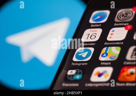 Smartphone-Bildschirm mit verschiedenen Anwendungssymbolen. Im Hintergrund ein verschwommenes Telegram-Logo. Stockfoto