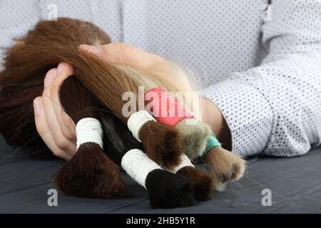 Mann hält in den Händen verschiedene Arten von Haar.Blonde, rote und braune Haarteile.Haarverlängerung Konzept. Stockfoto