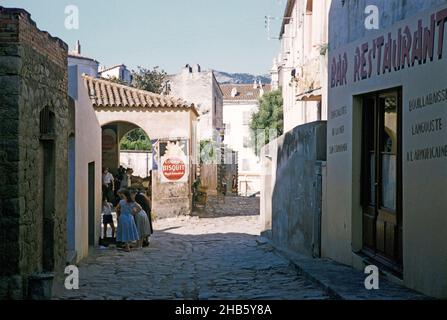 Menschen und Bars schmale Straßen in der historischen Zitadelle Stadt Calvi, Korsika, Frankreich in den späten 1950er Jahren Stockfoto