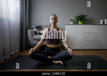 Junge Frau, die im Winter zu Hause meditiert Stockfoto