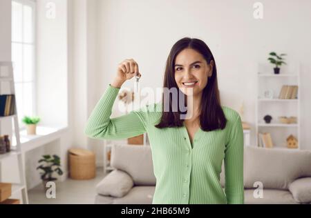 Porträt einer glücklichen, schönen jungen Hausbesitzerin, die Schlüssel zu ihrem neuen Zuhause zeigt. Stockfoto