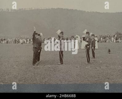 Vereidigung von Offizieren, Vereidigung einer Gruppe von drei Offizieren auf freiem Feld. Ein Offizier nimmt den Eid mit erhobener Hand ab. In der Nähe stehen einige Frauen, aus der Ferne mehr Publikum. Kleines Foto in einem Album von 87 Fotos über den Bau der Gajo-Straße auf Nord-Sumatra zwischen Bireuen und Takinguen zwischen 1903-1914., anonym, Noord-Sumatra, 1903 - 1913, fotografische Unterstützung, Höhe 78 mm × Breite 102 mm Stockfoto