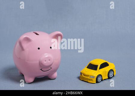 Konzept Akkumulation und Rettung.Sparschwein und gelbes Auto auf grauem Hintergrund Stockfoto