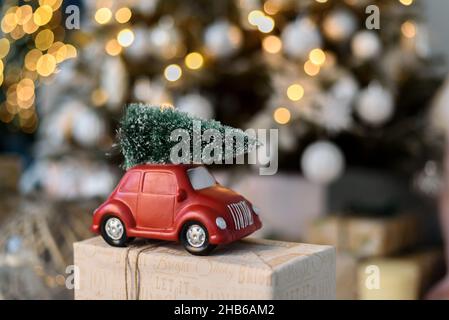 Unbekanntes rotes Spielzeugauto mit Weihnachtsbaum auf dem Dach, der auf der Geschenkbox steht Stockfoto