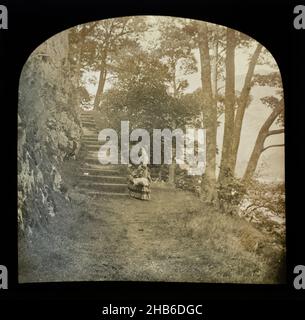 Magische Laternenrutsche der Frau, die in der Landschaft neben einem Treppenflug durch Wald steht, möglicherweise der Lake District, England, Großbritannien c 1900 Stockfoto