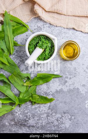 Frischer Bärlauch, auch bekannt als Bärlauch oder Ursinum-Allium-Pesto, in einem Mörser zerkleinert und Öl auf einem Stein, Betonstruktur Hintergrund und beigefarbenes Kätzchen Stockfoto