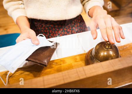 Weibliche Finger drücken die Klingel mit Pass und Gesicht auf die Hände der Rezeption im Hotel. Reisesicherheit und Einschränkungen während der Corona-Pandemie.2020 Stockfoto