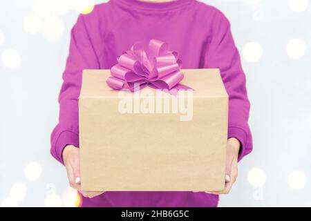 Geschenke in den Händen der Frau. Express-Lieferung. Eine junge Frau in einem violetten Sweatshirt hält eine Pappschachtel mit Schleife. Stockfoto